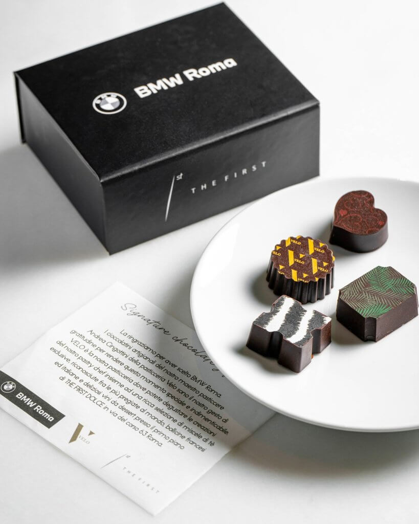 La scatola nera «BMW Roma / The First», un piatto con quattro cioccolatini decorati e la card «Signature tasting dinner», The First e BMW Roma, Lion Brand