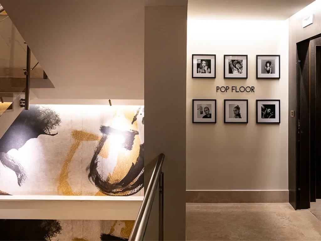 La scala e il corridoio «POP FLOOR» con i ritratti, l'ascensore e un quadro astratto, The First Musica, Lion Brand