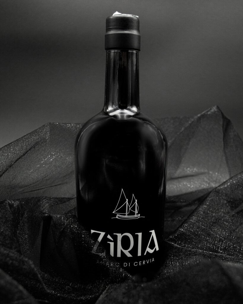 La bottiglia in piedi fra pieghe di tulle nero, il marchio bianco stampato sul vetro, Zìria, Lion Brand